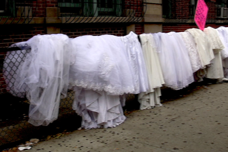 Many wedding dresses hanging from a railing.