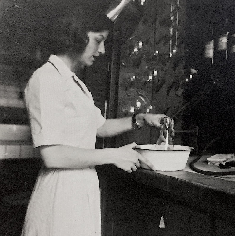 Black and white photo of a young white woman standing at a bench  in a laboratory.