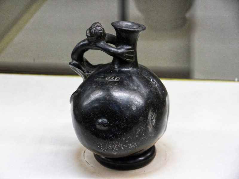 Black pre-Columbian ceramic jug in the shape of a potato with a monkey as the handle.