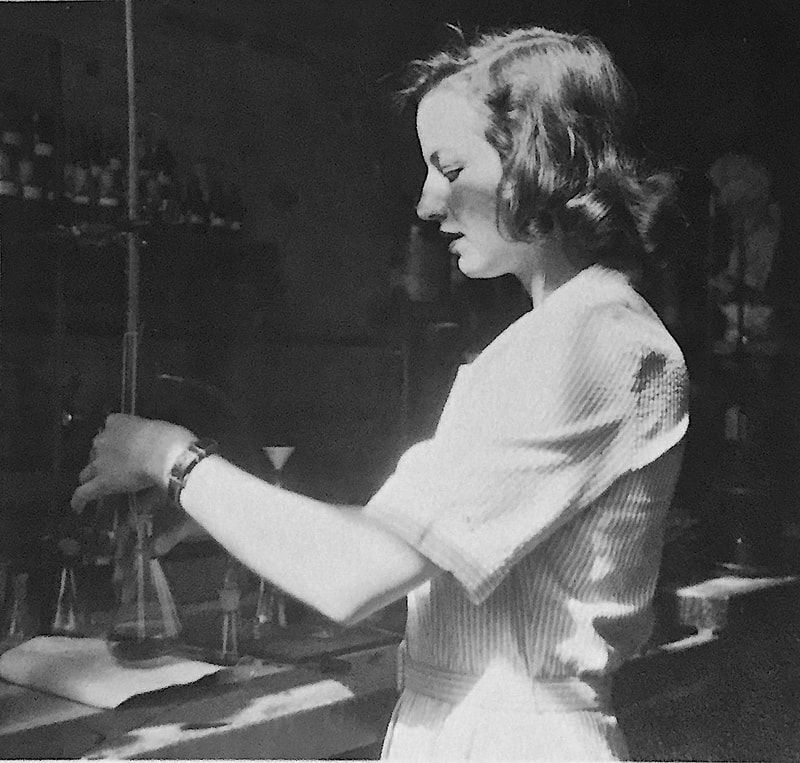 Black and white photo of a young white woman working at a bench in a laboratory.