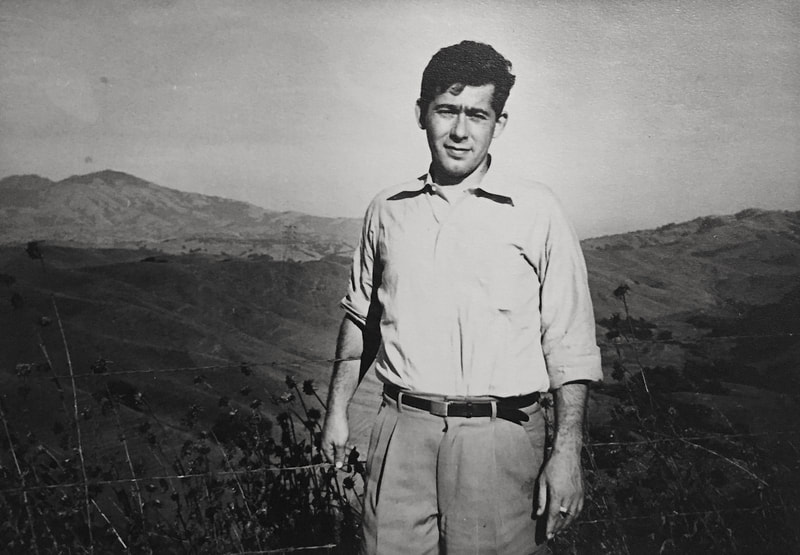 Black and white photo of a young white man standing in front of a vista of mountains.