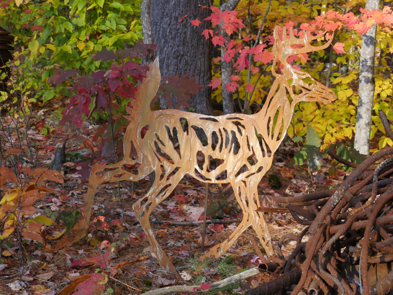 A large steel silhouette of a deer in front of trees and bushes in autumn.